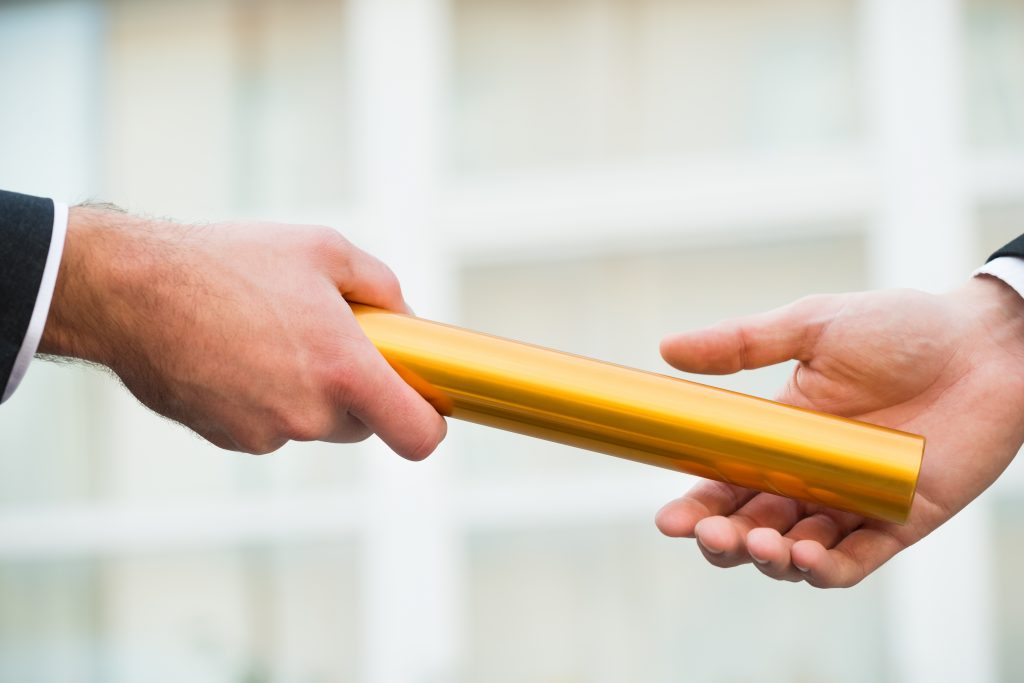 Cropped hand of businessman giving golden relay baton to colleague outdoors