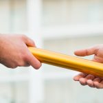 Cropped hand of businessman giving golden relay baton to colleague outdoors